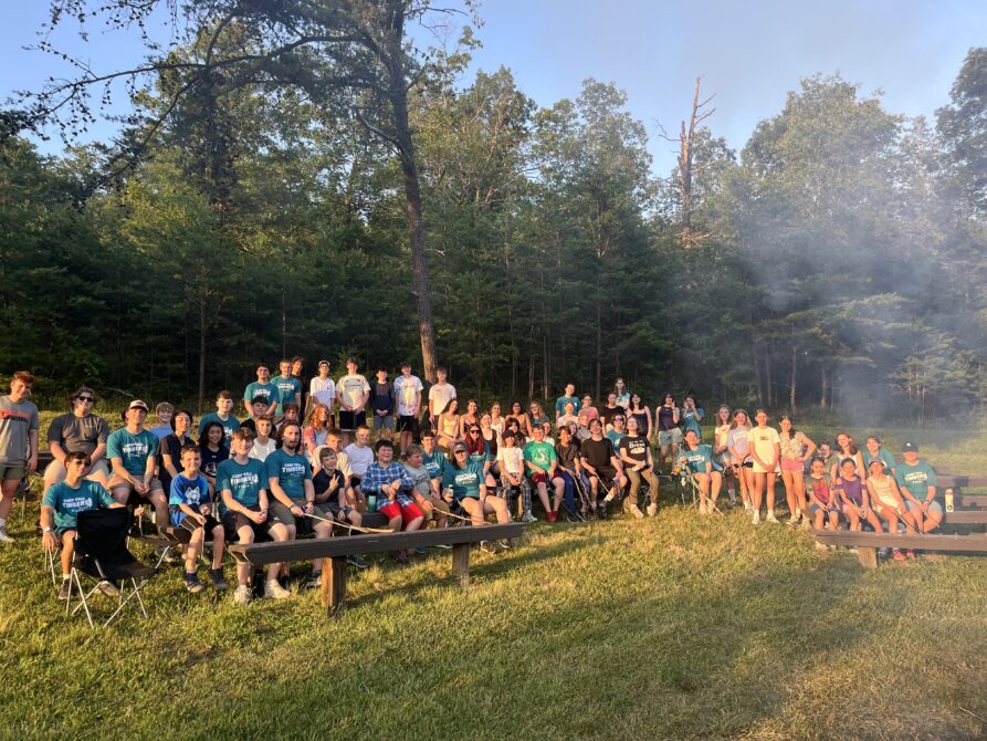 A group of around 50 children and counselors around a fireplace at Camp Tall Timbers overnight summer camp.