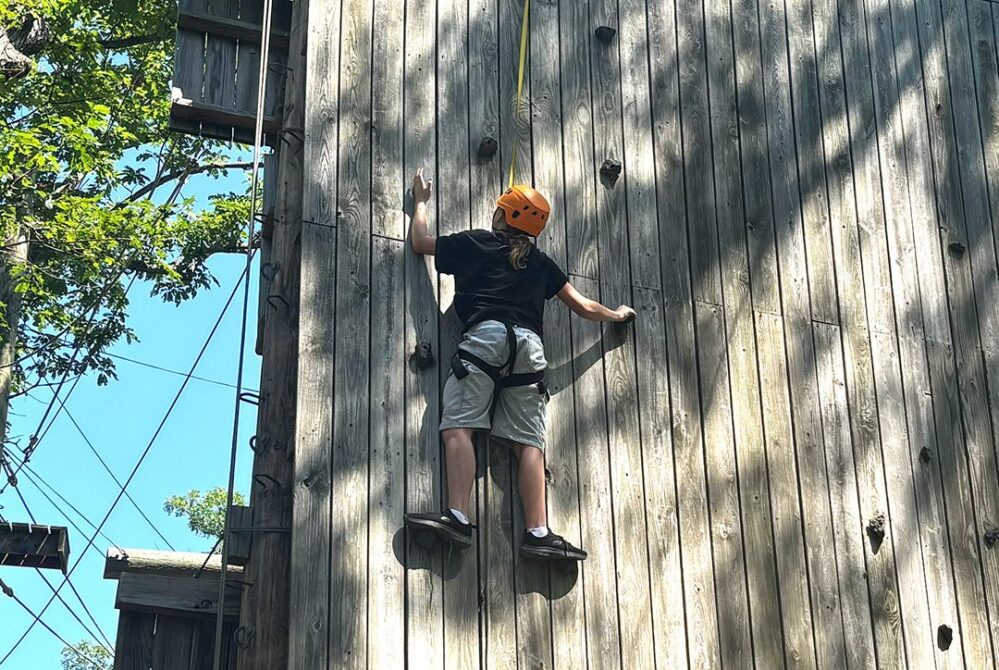 A camper climbing the wooden climbing wall